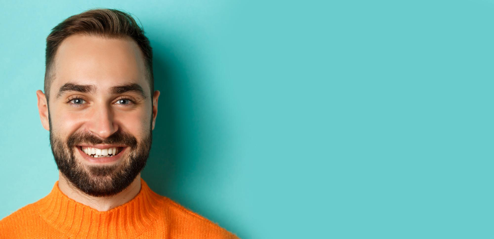 Headshot of handsome Caucasian man with beard smiling happy at camera standing in orange sweater